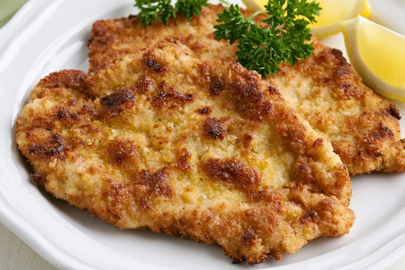 Two golden-brown breaded schnitzel cutlets on a white ceramic plate garnished with parsley and lemon slices