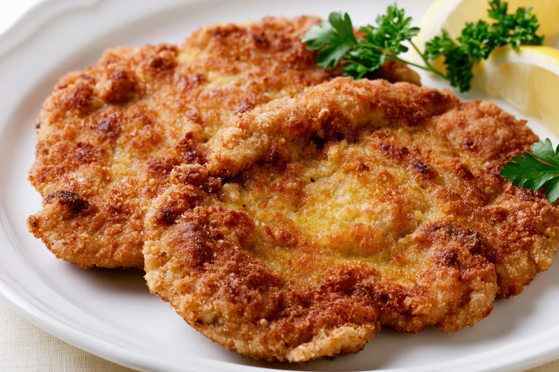 Two golden-brown breaded schnitzel cutlets on a white ceramic plate garnished with parsley and lemon slices