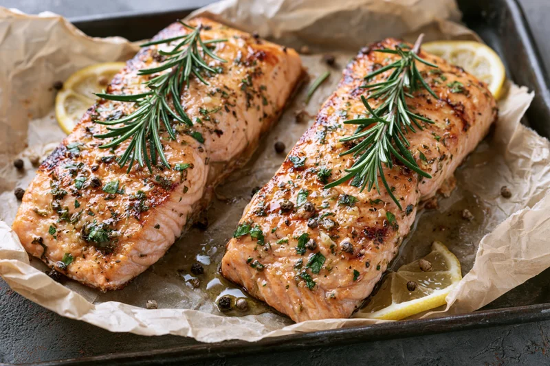 Two seared salmon fillets garnished with rosemary and lemon on parchment-lined baking tray