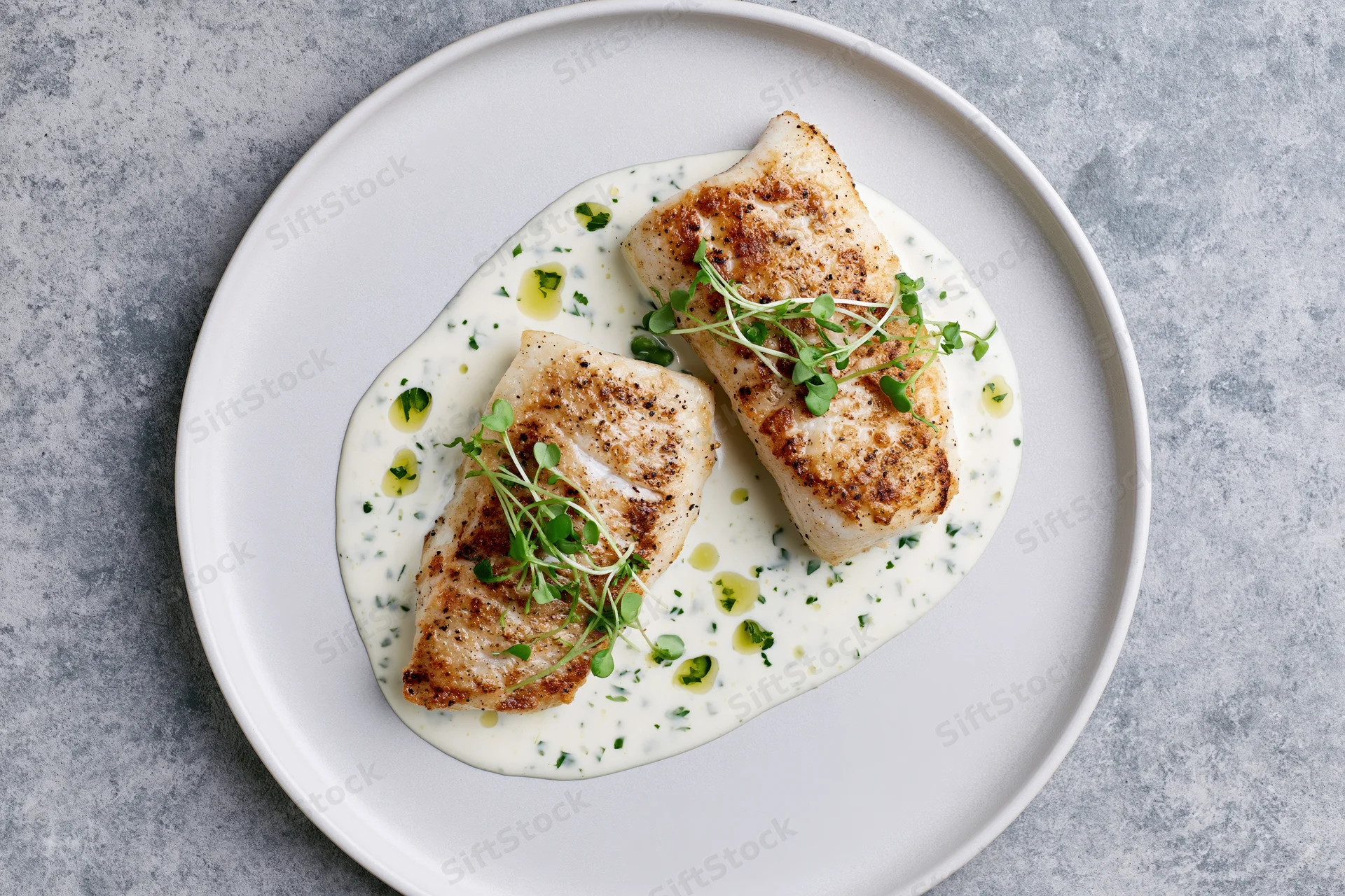 Two seared white fish fillets on a cream sauce with microgreens on a white plate