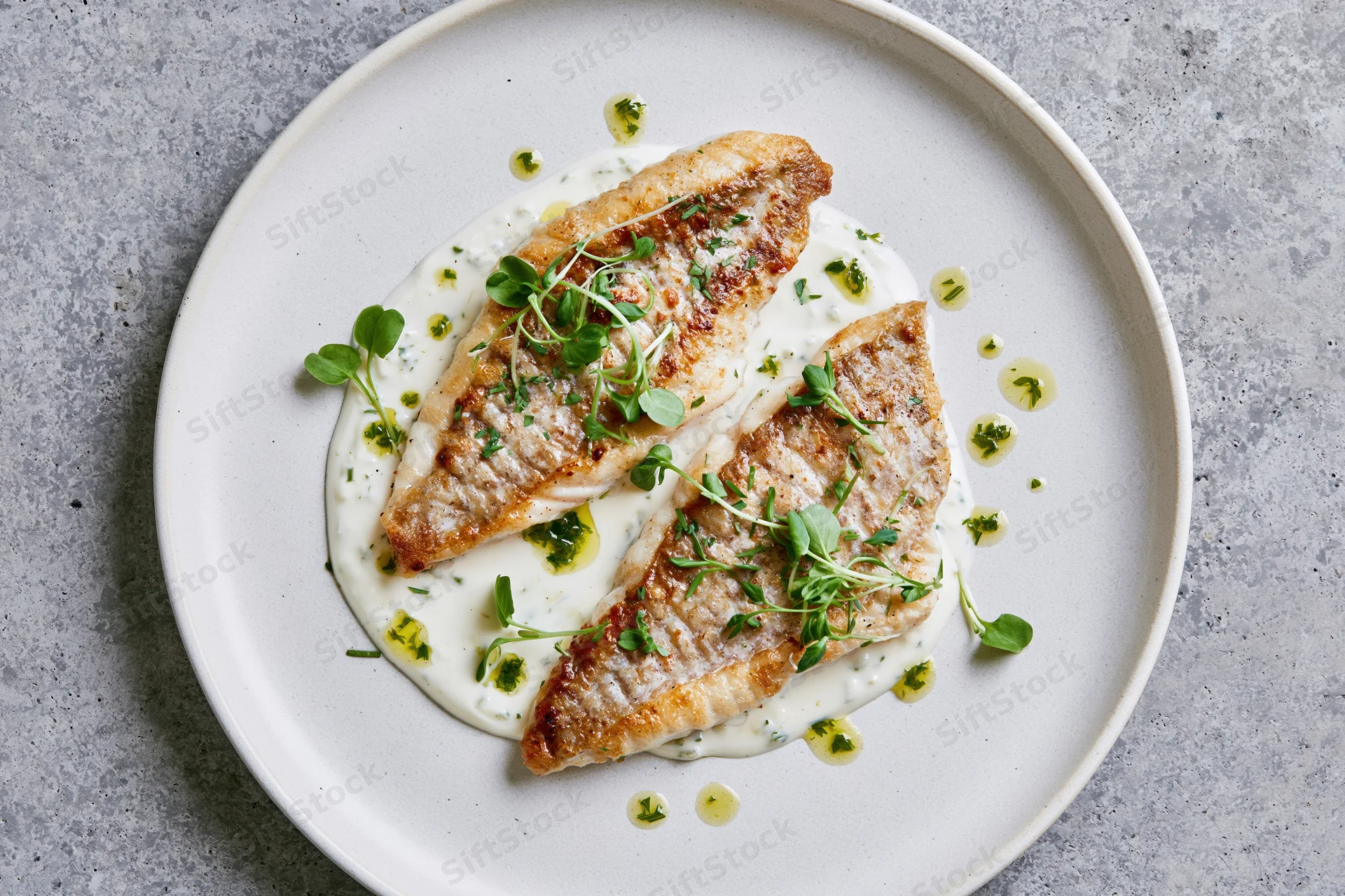 Two seared white fish fillets on a cream sauce with microgreens on a white plate