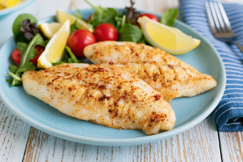Two pan-seared white fish fillets with salad and lemon wedges on a blue plate