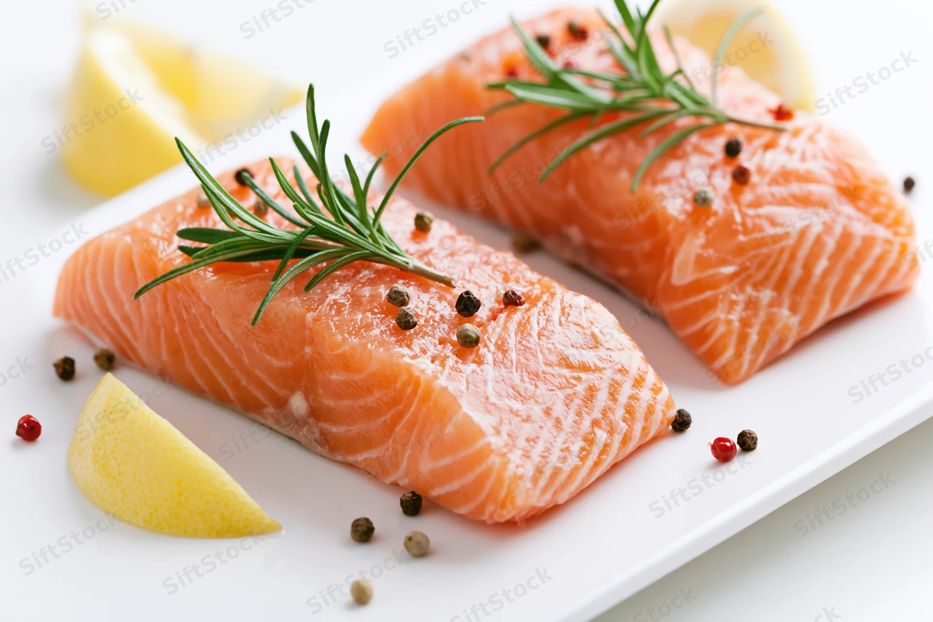 Two raw salmon fillets garnished with rosemary and lemon on a white plate