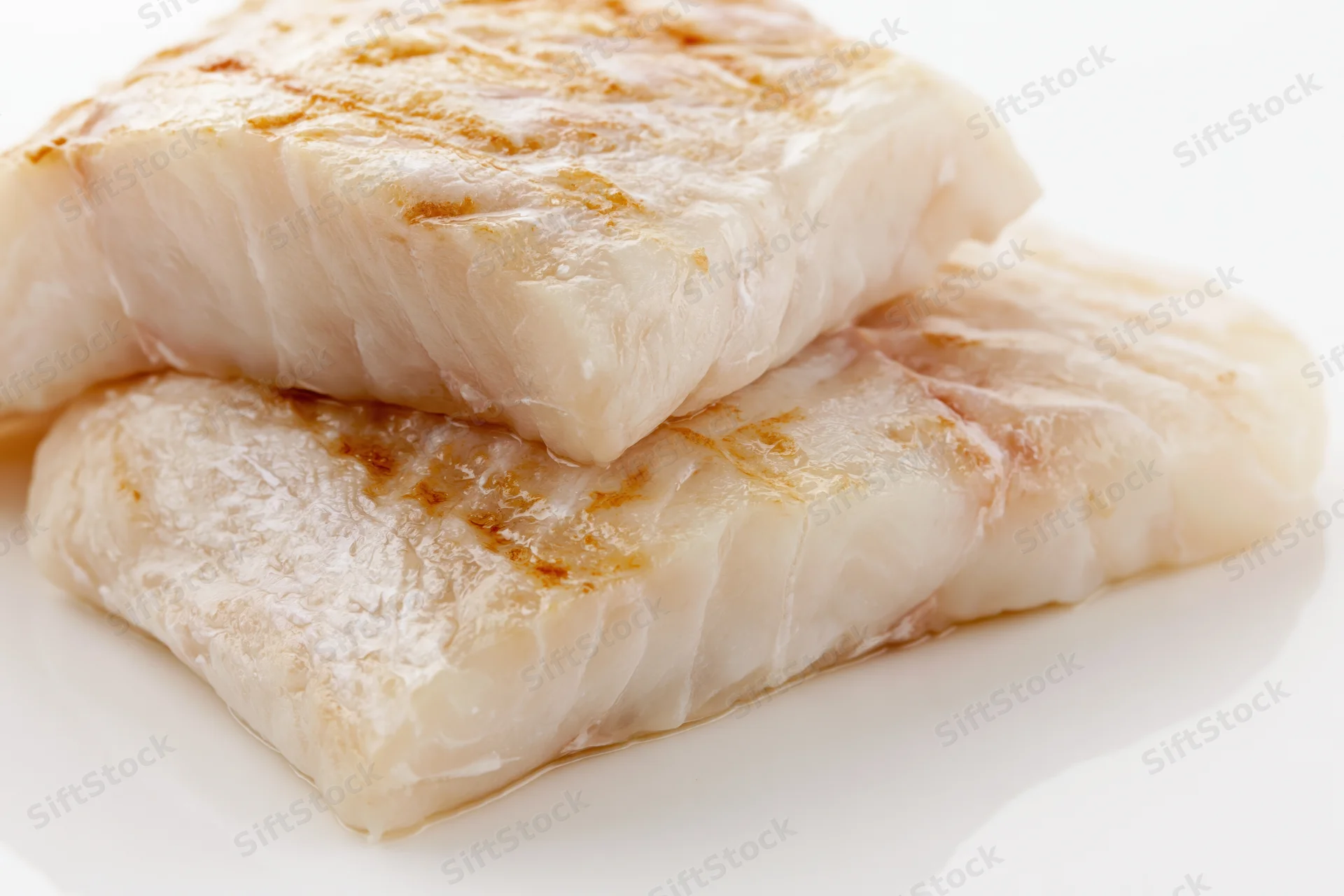Two raw white fish fillets stacked slightly offset on a white surface