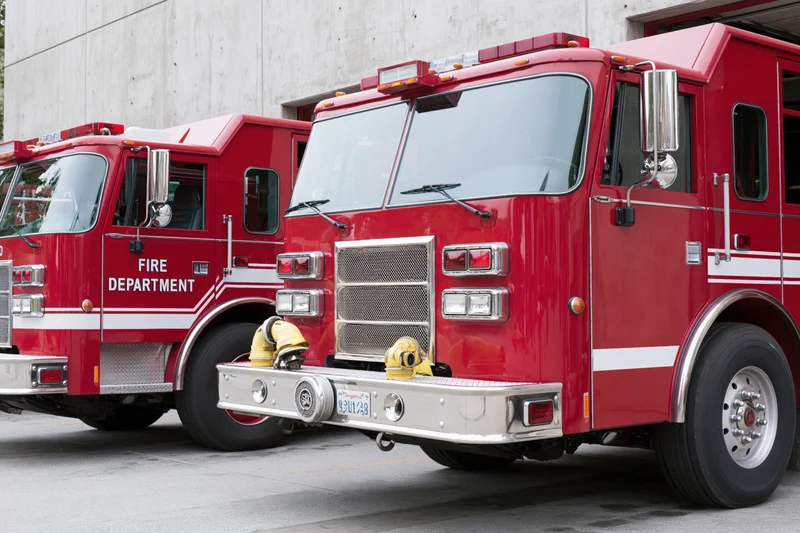 Two red fire department engine trucks parked side by side outside a station