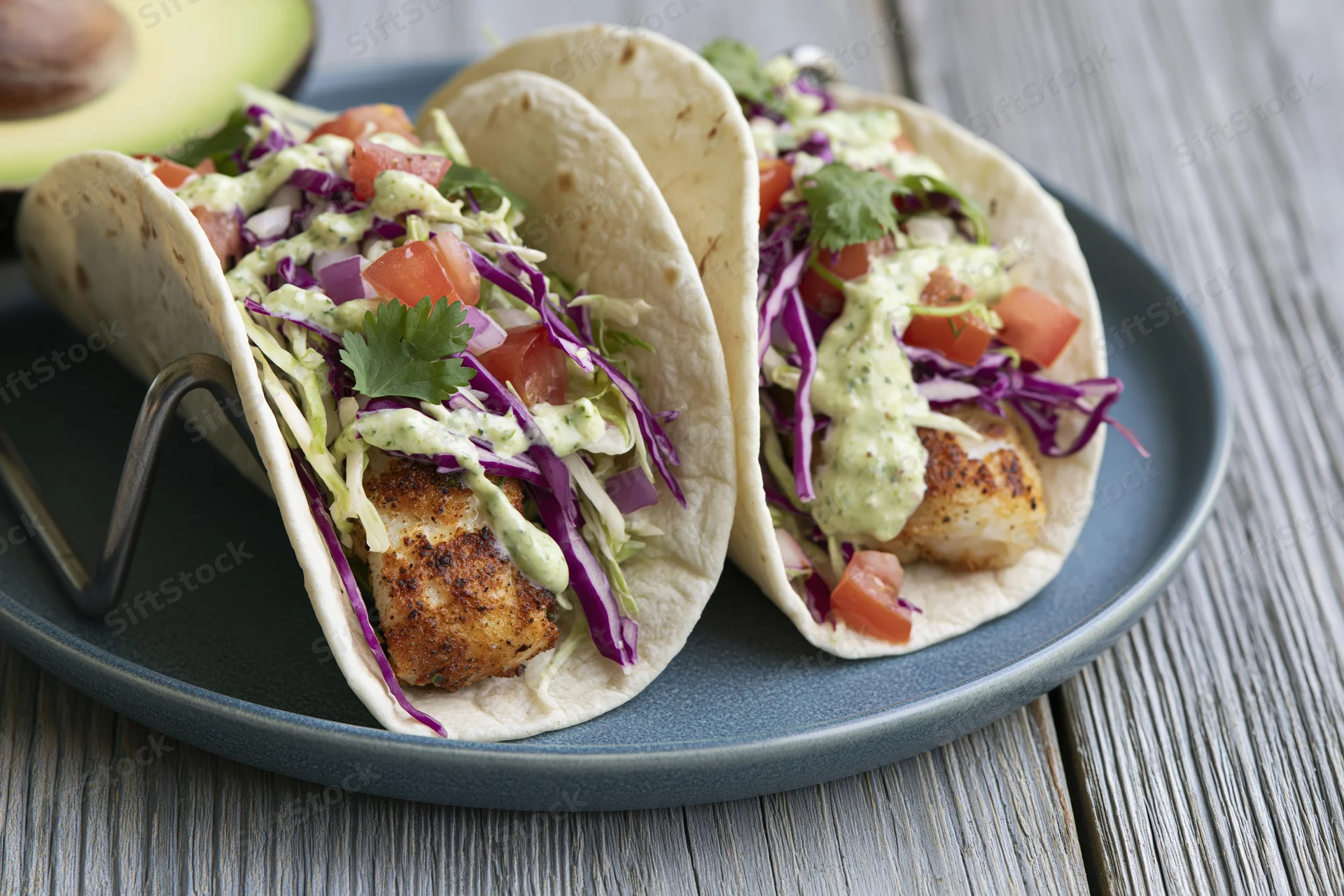 Two grilled fish tacos in soft flour tortillas with slaw and sauce on a blue plate on wooden table