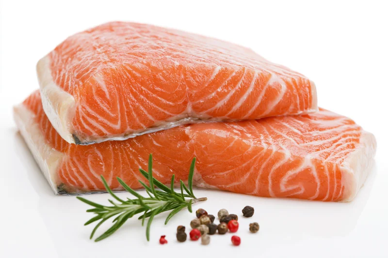 Two thick raw salmon fillets stacked with rosemary and peppercorns on white background