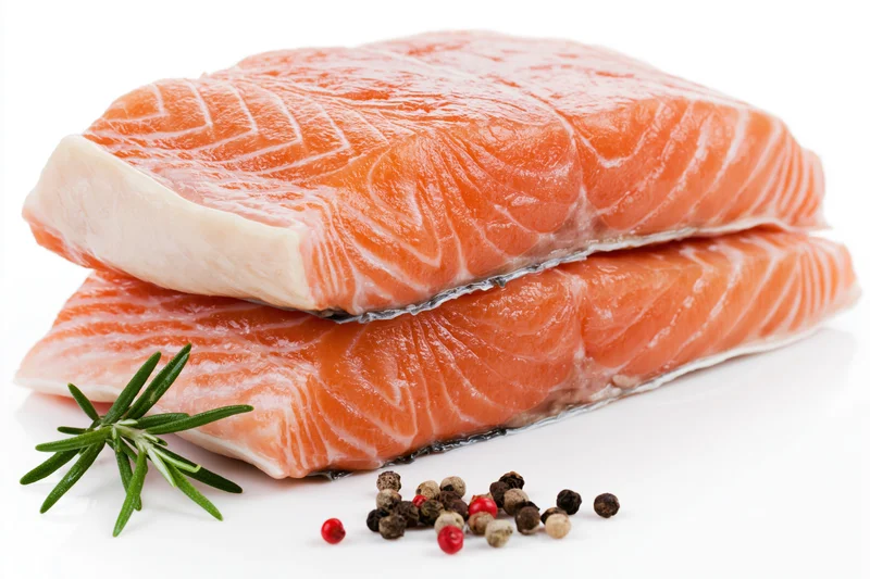 Two thick raw salmon fillets stacked on white background with rosemary and peppercorns
