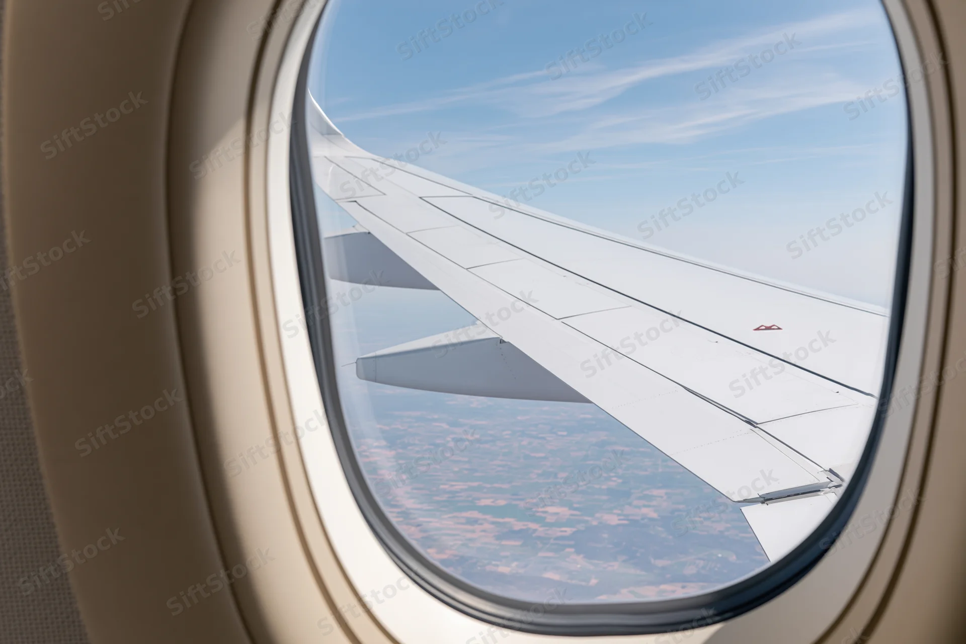 View through airplane window showing wing against blue sky and landscape below