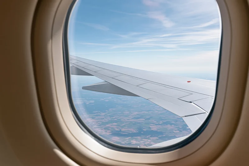 View through airplane window showing wing and sky above landscape