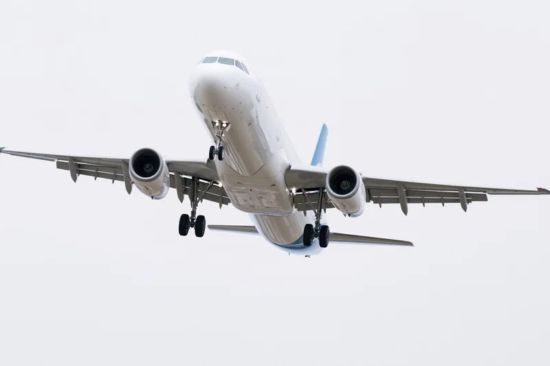 White and blue narrow-body commercial passenger jet approaching for landing against overcast sky