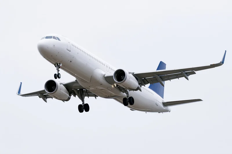 White and blue commercial passenger jet in landing approach against overcast sky