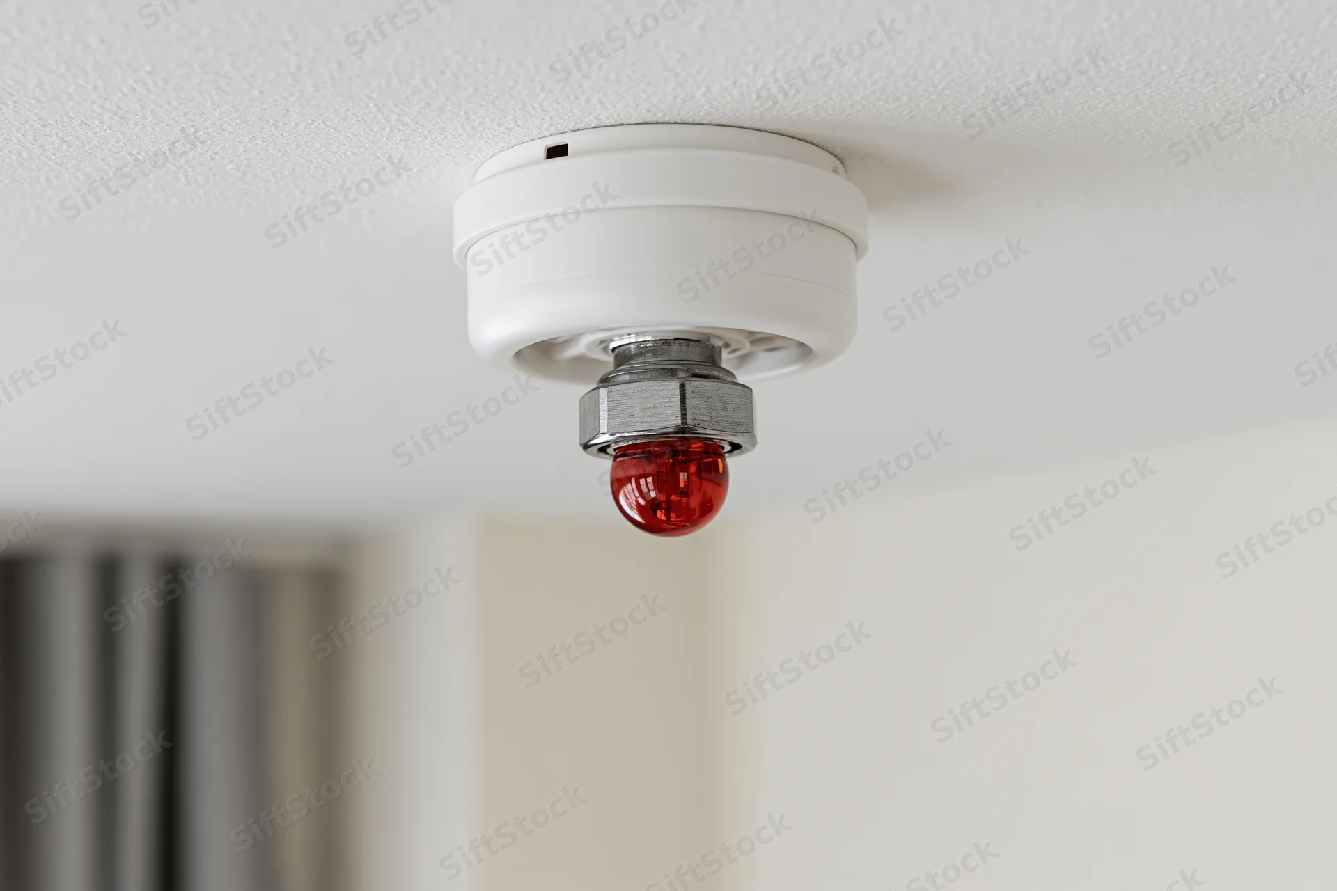 White smoke detector with red glass lens mounted on ceiling in indoor space