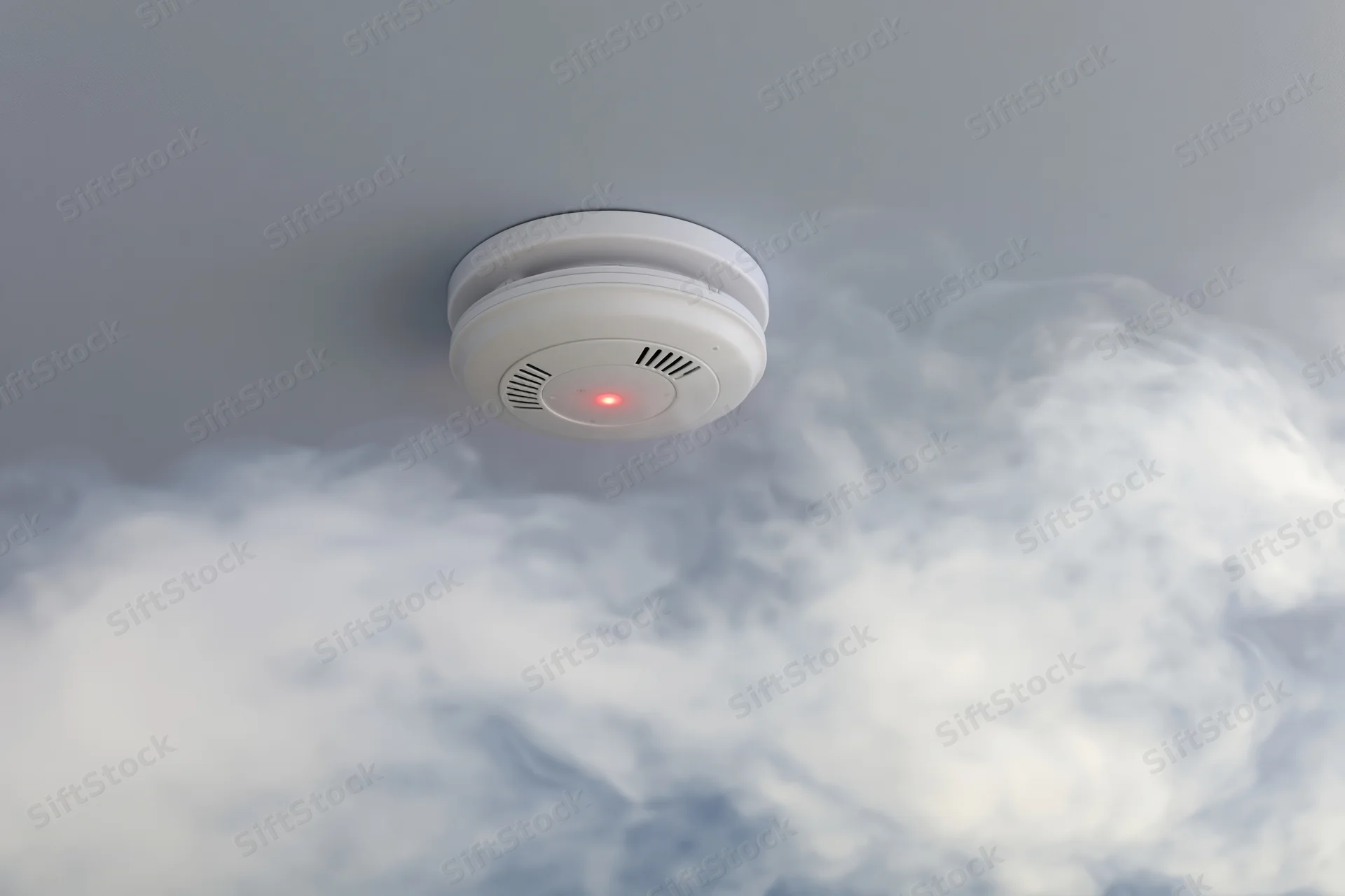 White smoke detector mounted on gray ceiling with smoke rising around it