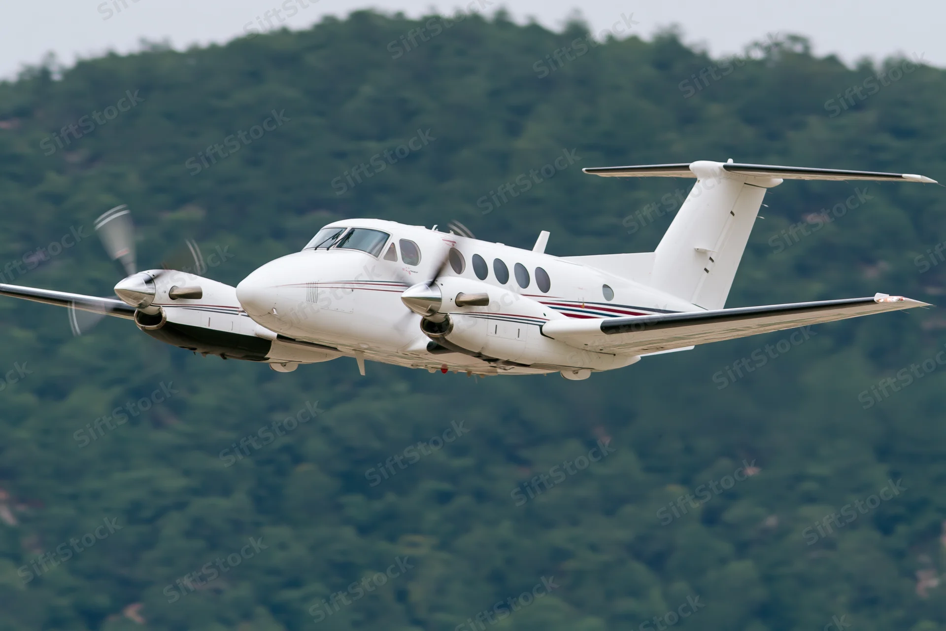 White twin-engine turboprop aircraft in low-altitude flight over forested mountains