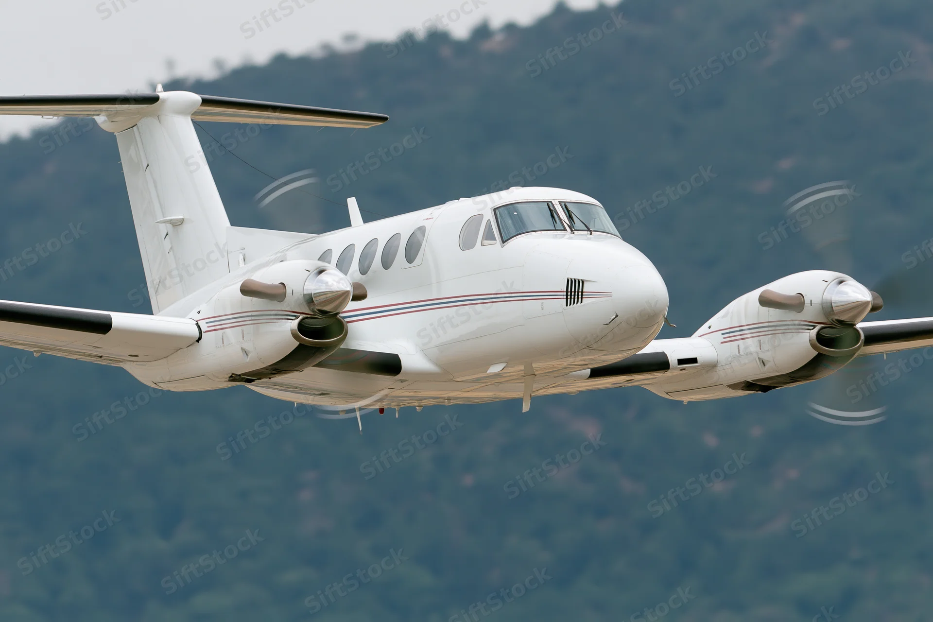 White twin-engine turboprop aircraft in low-altitude flight over mountainous terrain