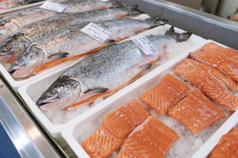 Whole fresh salmon and fillets arranged on crushed ice in a market display tray