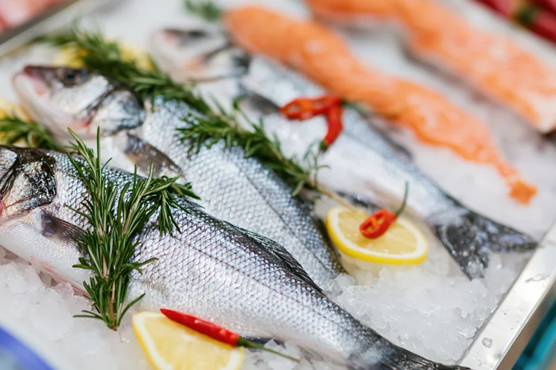 Whole fresh sea bass arranged on crushed ice with lemon and rosemary at a fish market