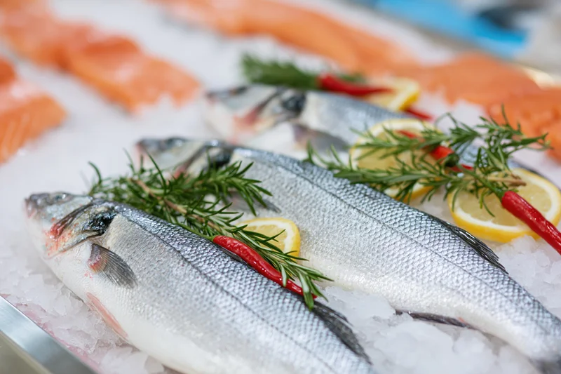 Whole fresh sea bass arranged on crushed ice with lemon and herbs at a fish market