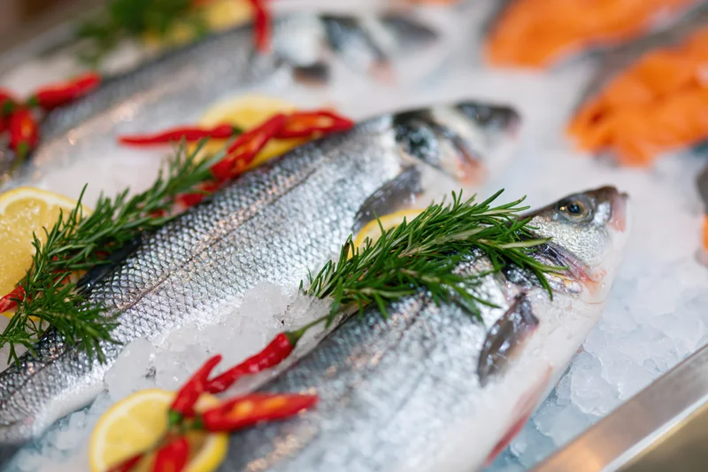 Whole fresh sea bass arranged on crushed ice with lemon, rosemary and chili at a fish market