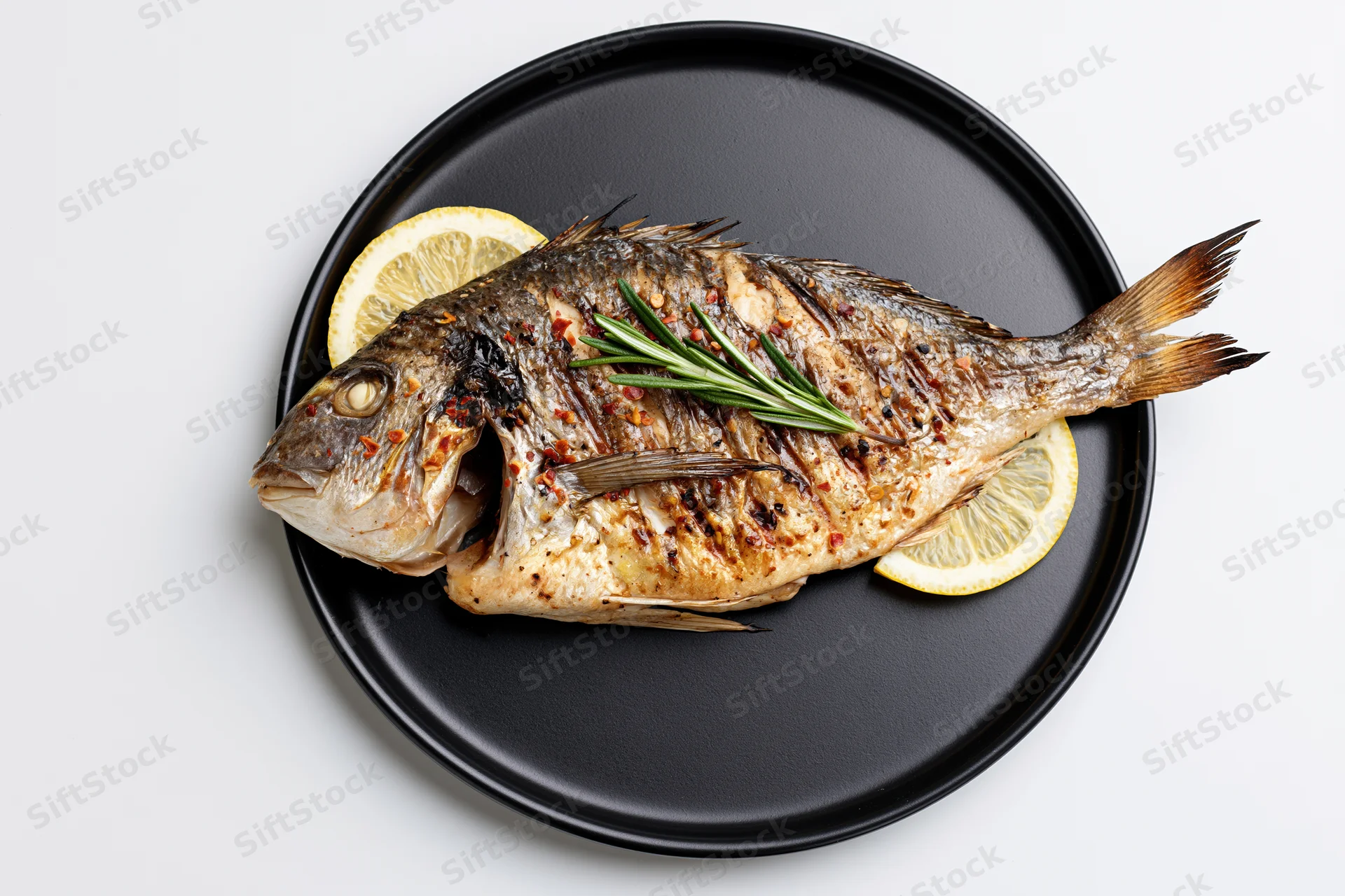 Whole grilled sea bream on a black ceramic plate with lemon and rosemary garnish