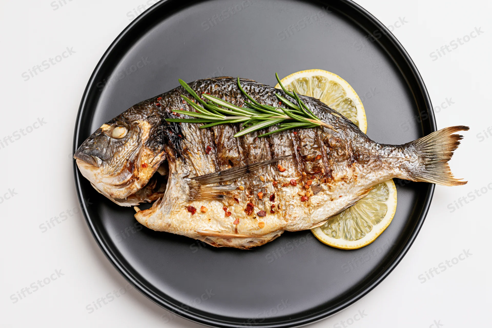 Whole grilled sea bream on a black ceramic plate with lemon and rosemary garnish
