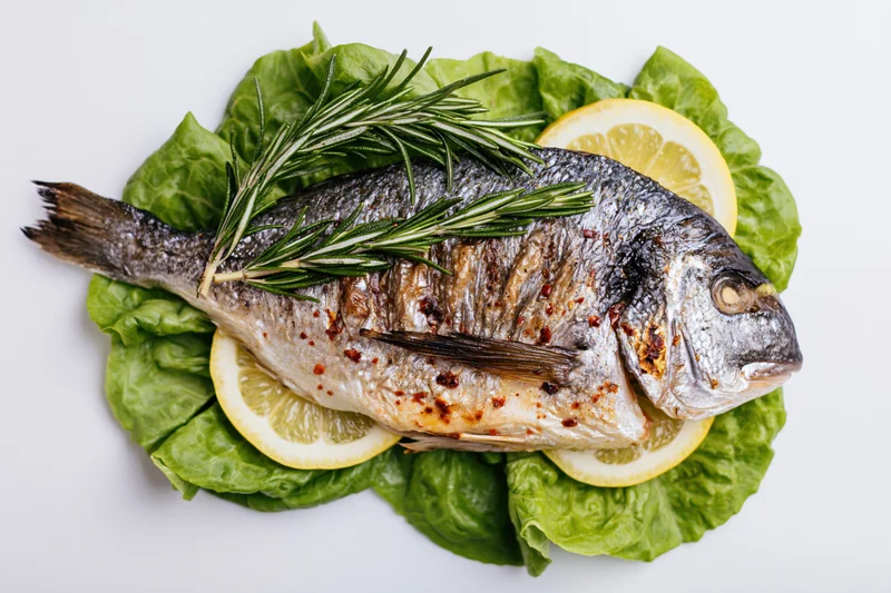 Whole grilled sea bream on fresh lettuce with lemon and rosemary garnish