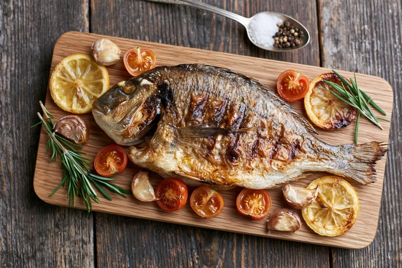 Whole grilled sea bream resting on a wooden cutting board