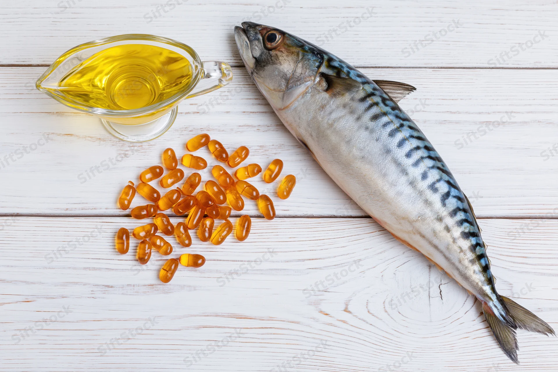 Whole raw mackerel fish lying on white wooden surface beside olive oil and omega-3 capsules
