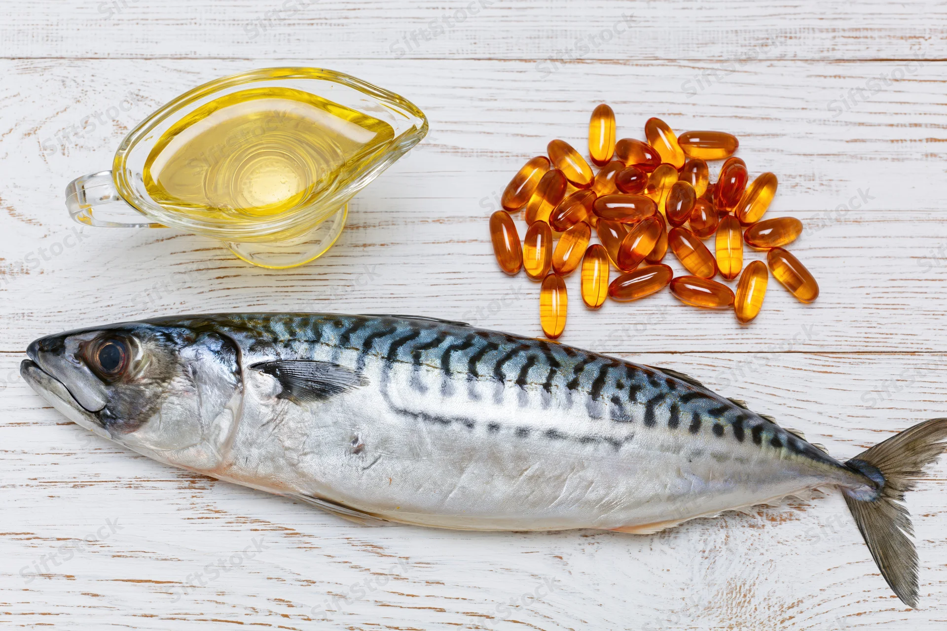 Whole raw mackerel fish lying on white-painted wooden surface with fish oil and omega-3 capsules nearby