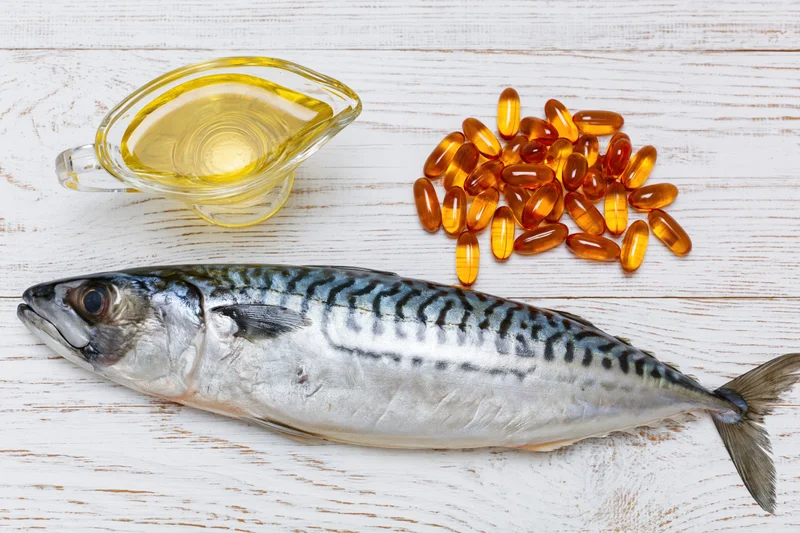 Whole raw mackerel fish lying on white-painted wooden surface with fish oil and omega-3 capsules nearby