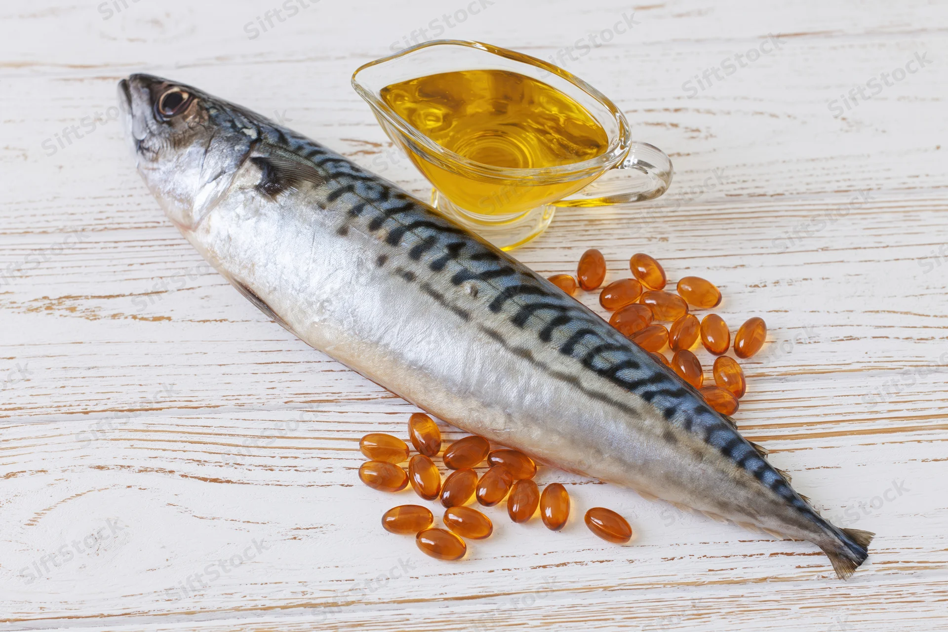 Whole raw mackerel fish lying on white wooden surface with fish oil capsules and glass pitcher of oil