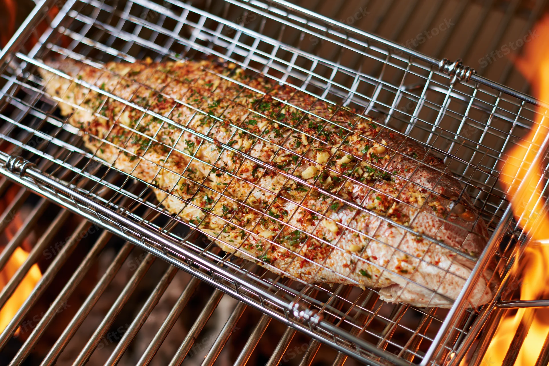 Whole seasoned fish in a wire basket grilling over open flames on a barbecue grill
