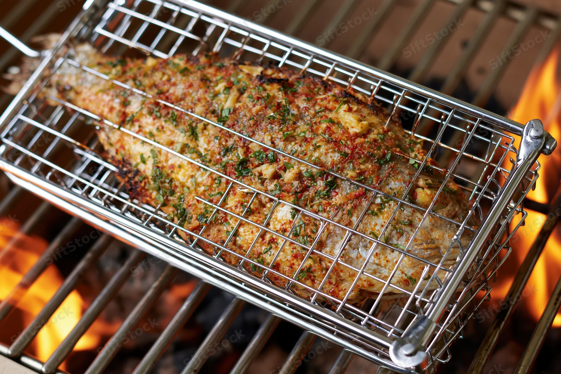 Whole seasoned fish in a wire basket grilling over open flames on a barbecue grill