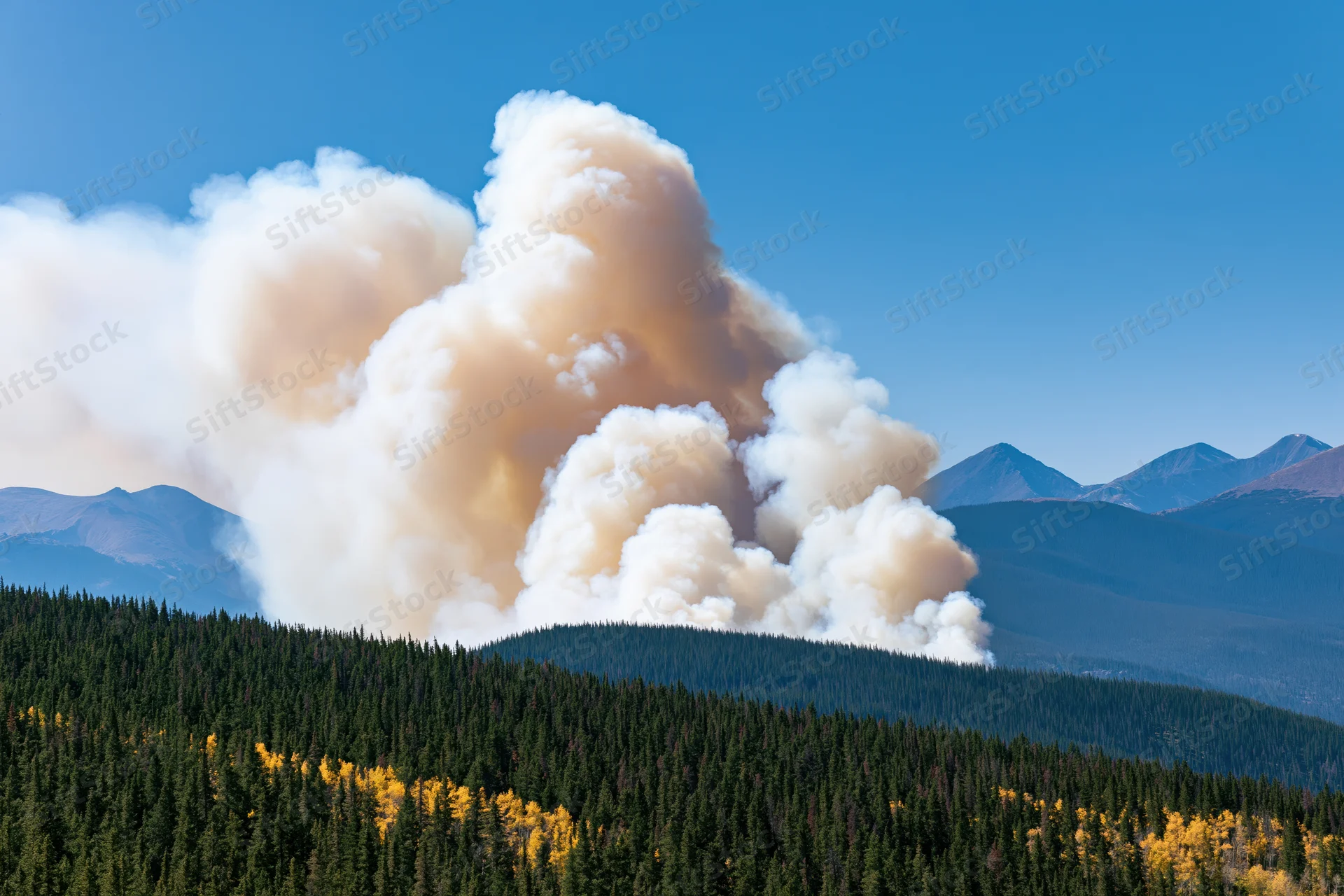 Thick smoke rising from a wildfire burning along a forested mountain ridge under a clear blue sky