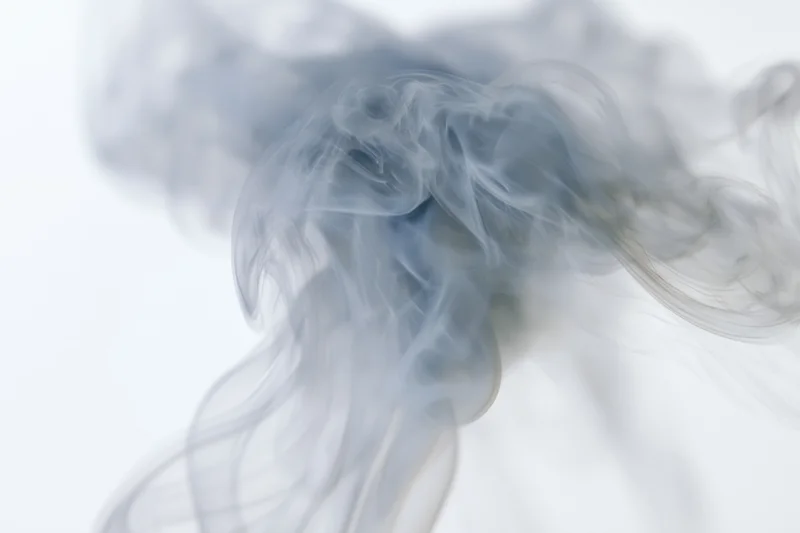 Wispy smoke curling and dispersing upward against a plain white background