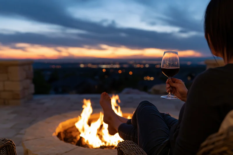 Woman seen from behind relaxing with wine by a fire