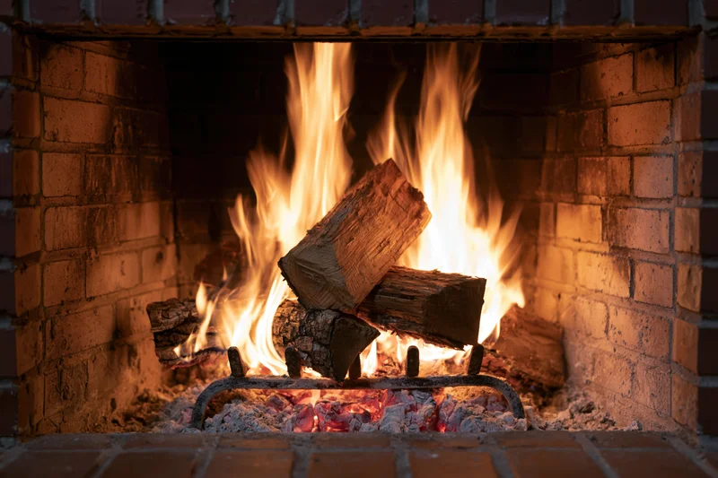 Wood logs burning in a brick fireplace with flames and embers visible