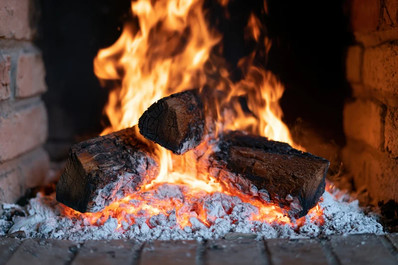 Burning wood logs in a brick fireplace with rising flames and glowing embers