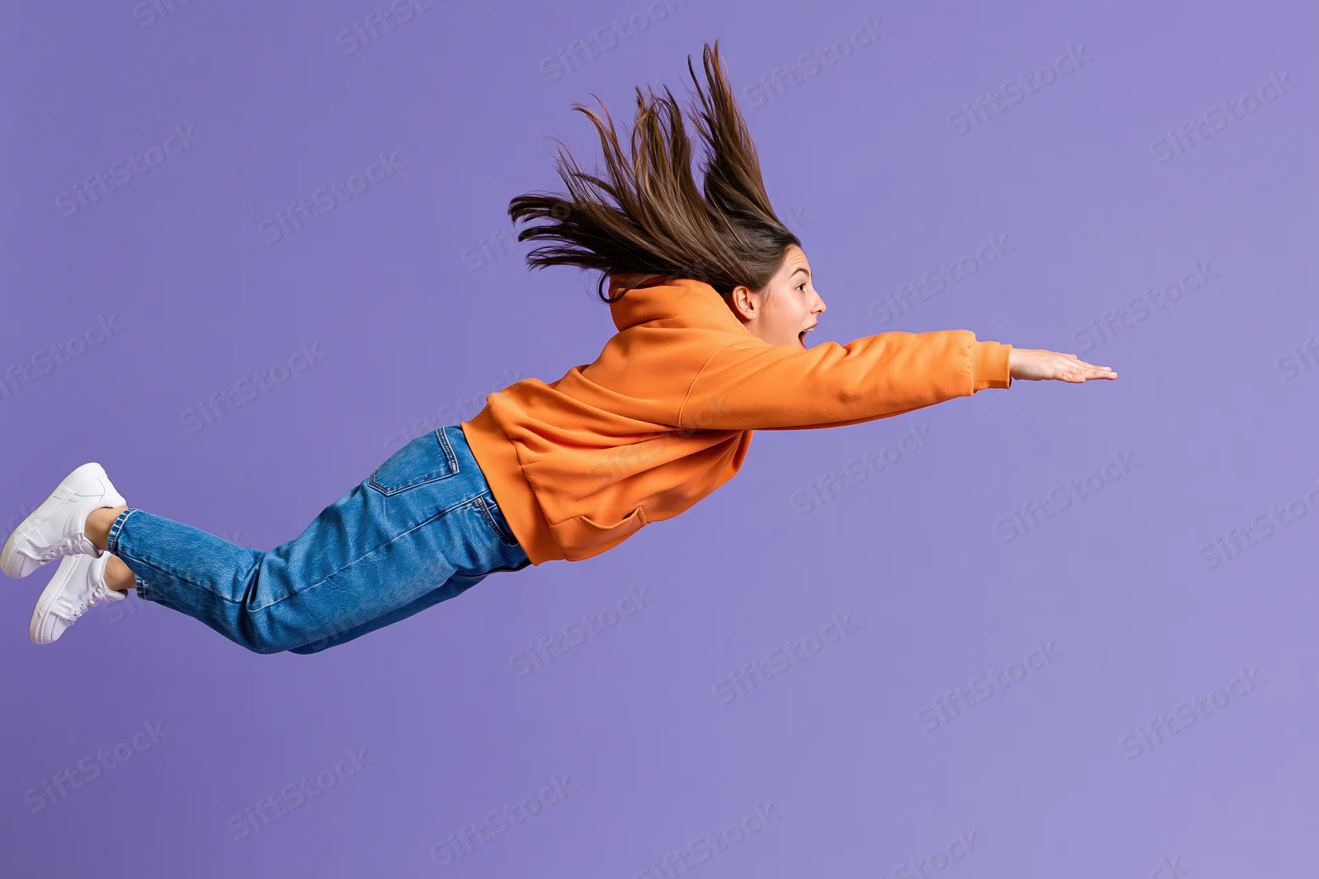 Young woman mid-jump in horizontal pose against purple studio background