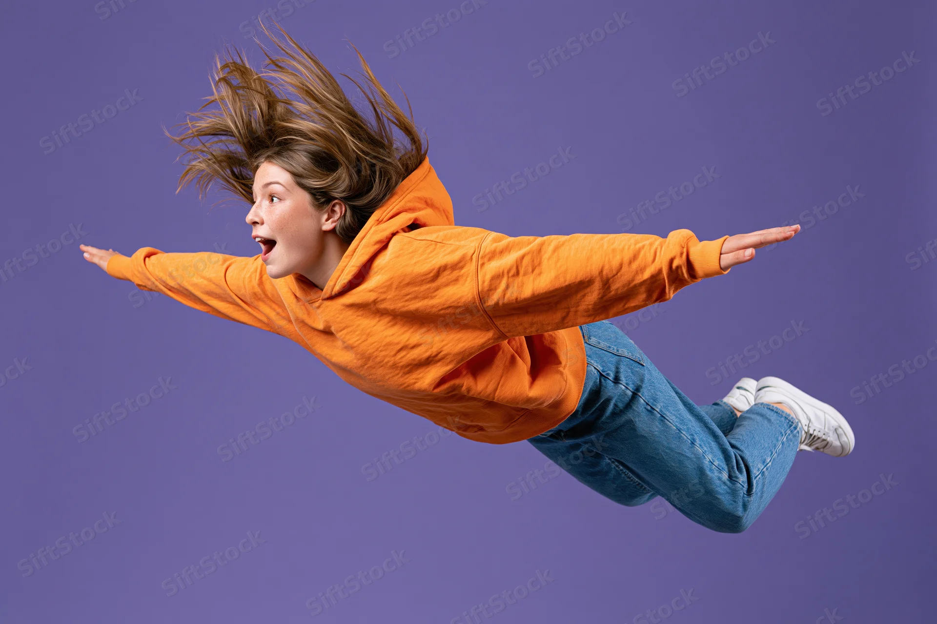 Young woman mid-jump in orange hoodie and jeans against purple background