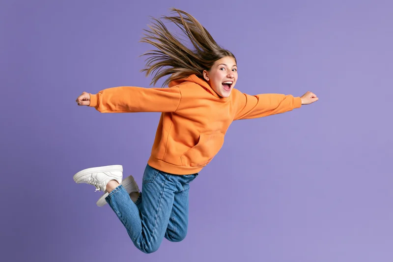 Girl jumping midair with arms outstretched against purple background