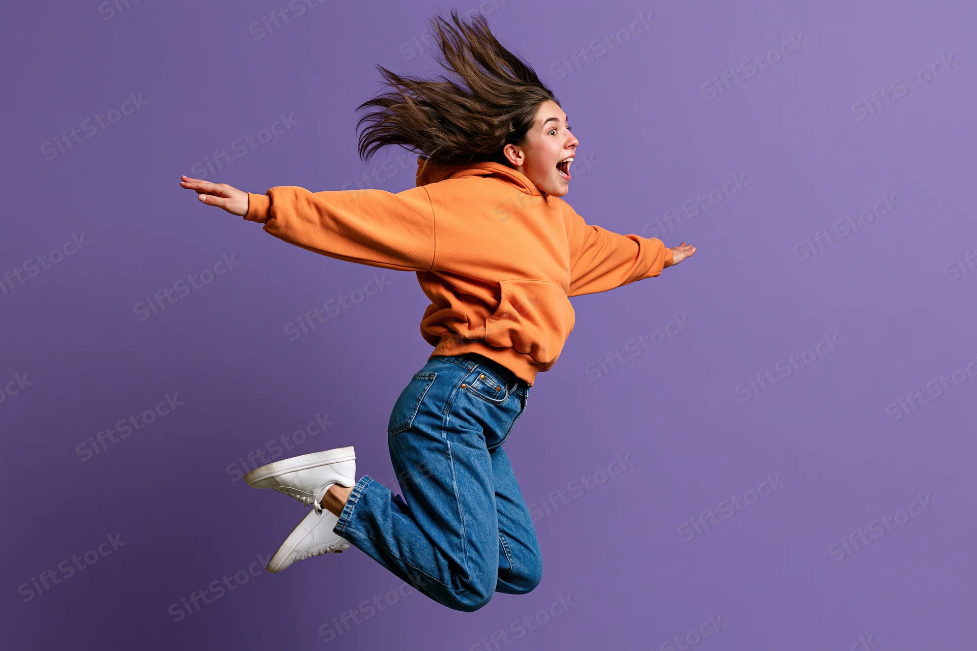 Young woman jumping midair with arms outstretched against purple studio background
