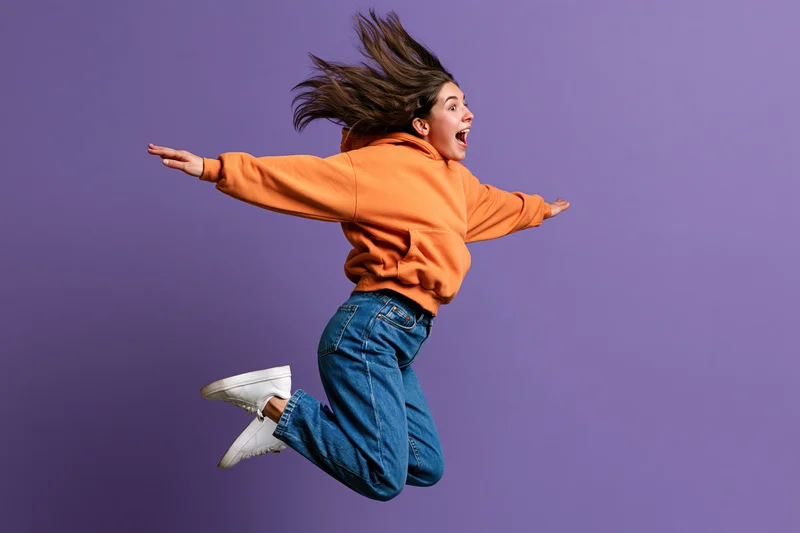 Young woman jumping midair with arms outstretched against purple studio background