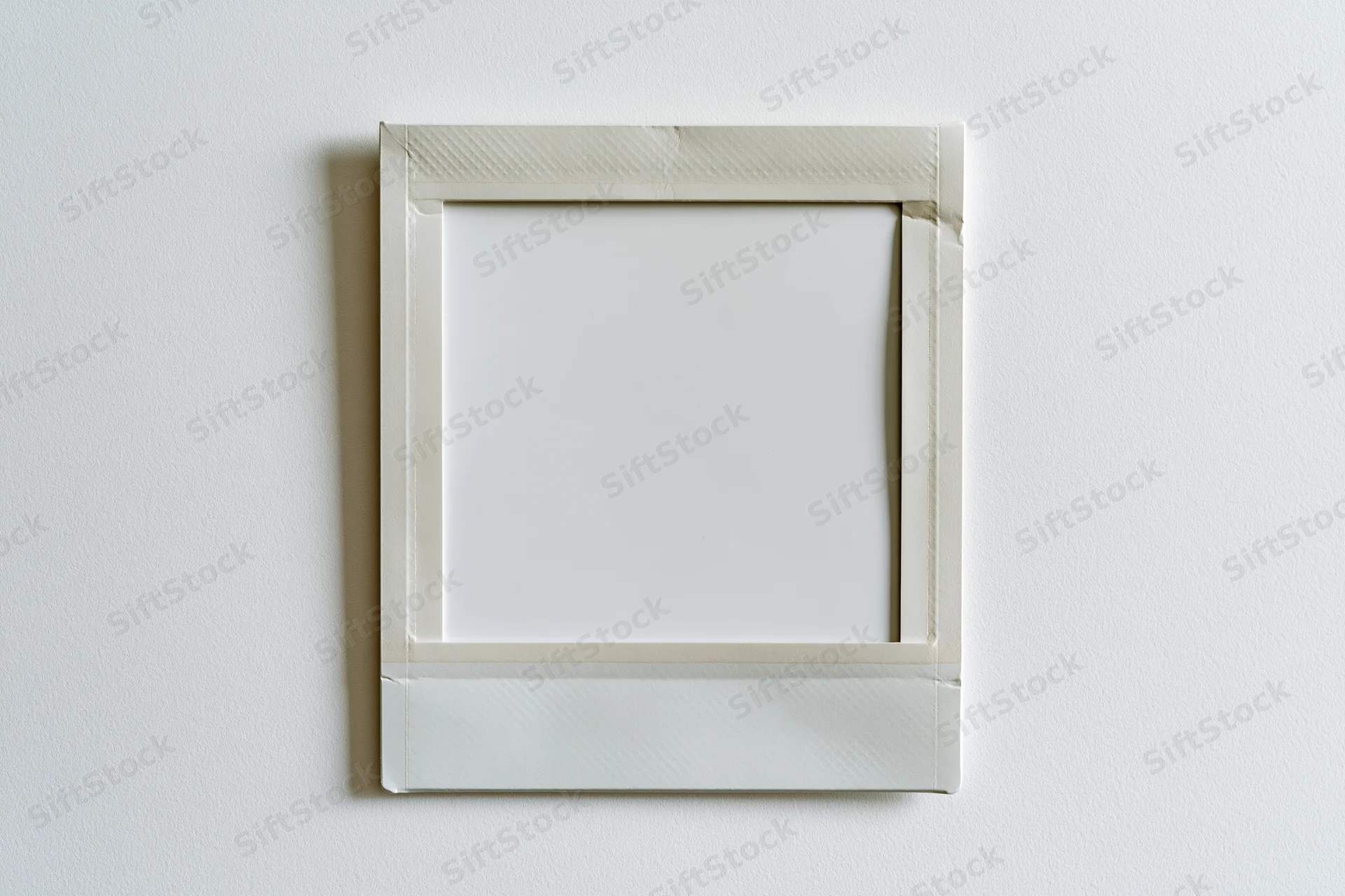 Blank instant film print with white border hanging on a plain wall