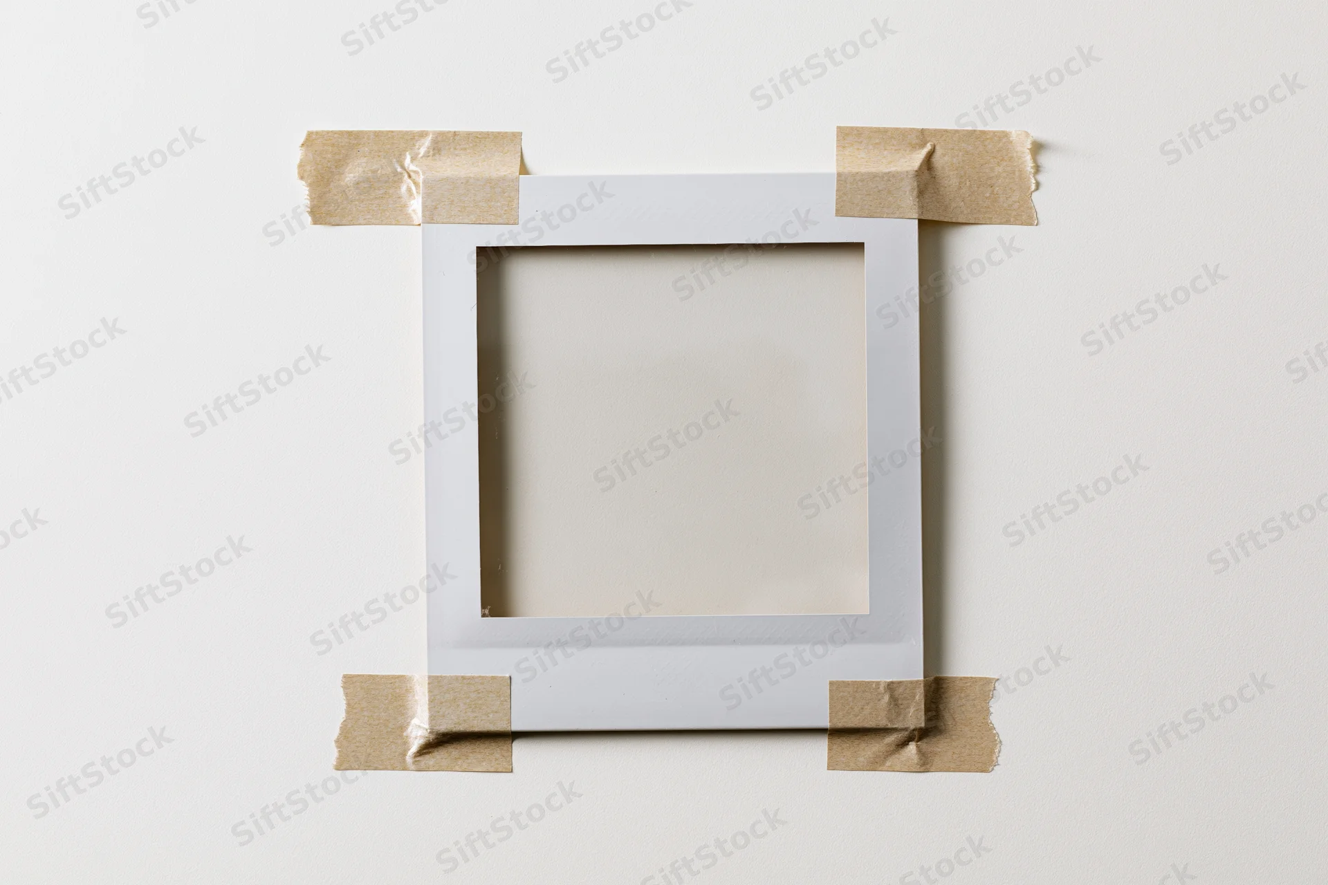 Blank polaroid frame taped to white surface with craft tape