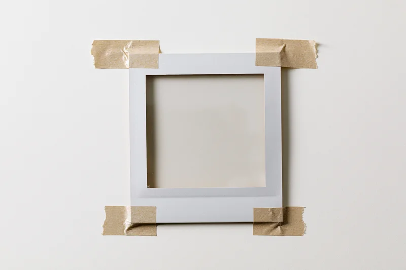 Blank polaroid frame taped to white surface with craft tape