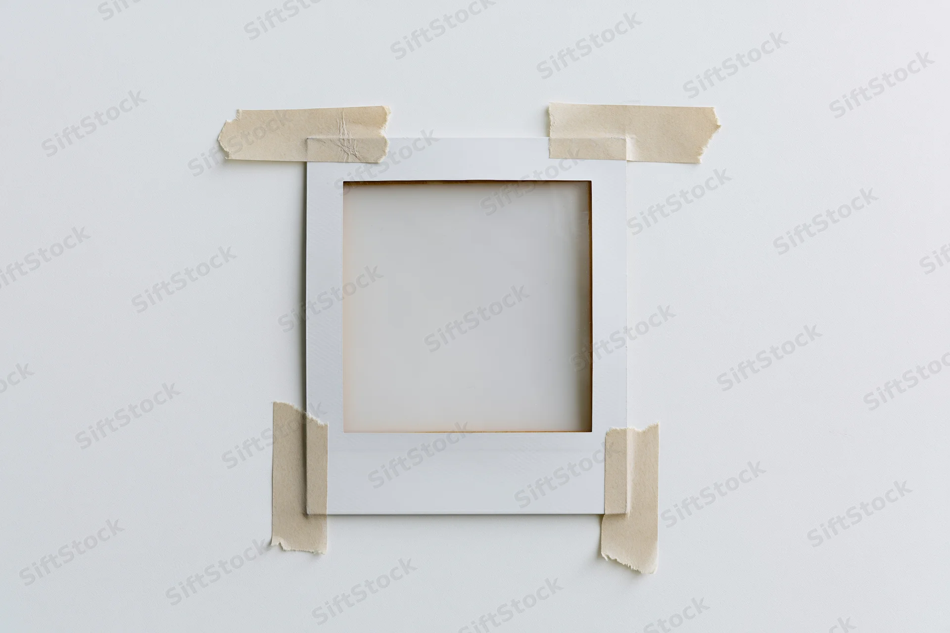 Blank polaroid frame taped to white surface with beige adhesive tape, centered, flat lay view