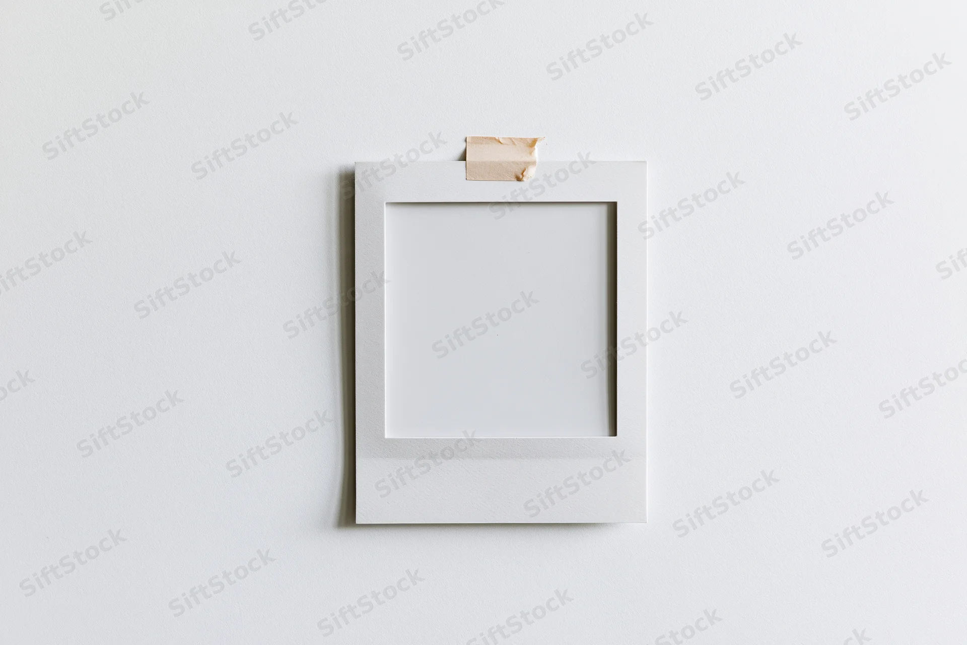 Blank white polaroid photo print taped to a white wall