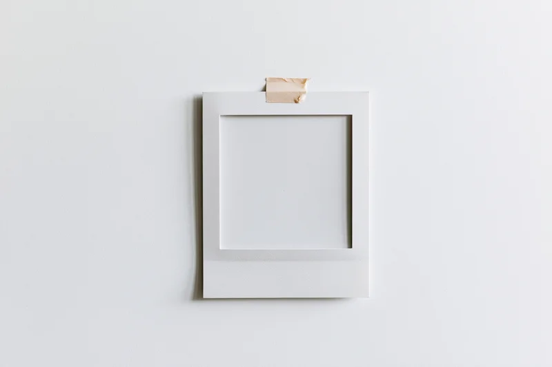 Blank white polaroid photo print taped to a white wall